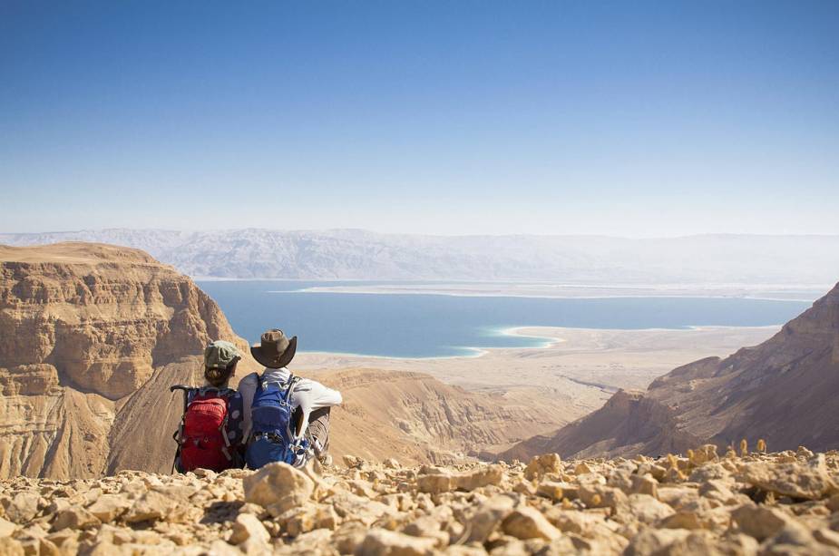 Um casal de viajantes observando o Mar Morto do topo de uma colina